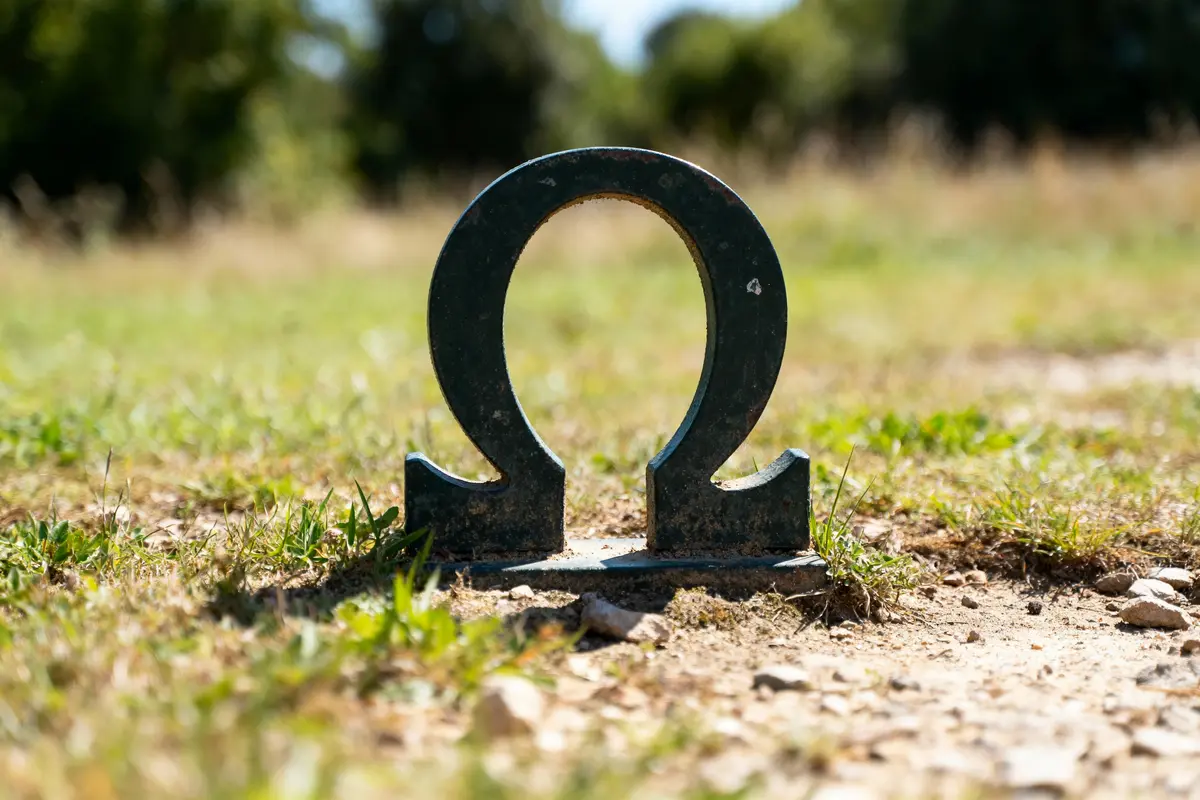Symbole Oméga métallique planté dans l'herbe, en plein air et éclairé par le soleil.
