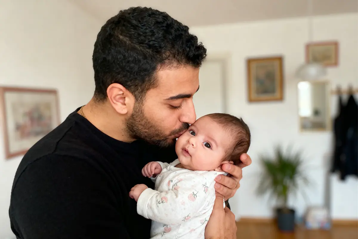 Un homme embrasse tendrement un bébé dans un intérieur chaleureux et décoré.